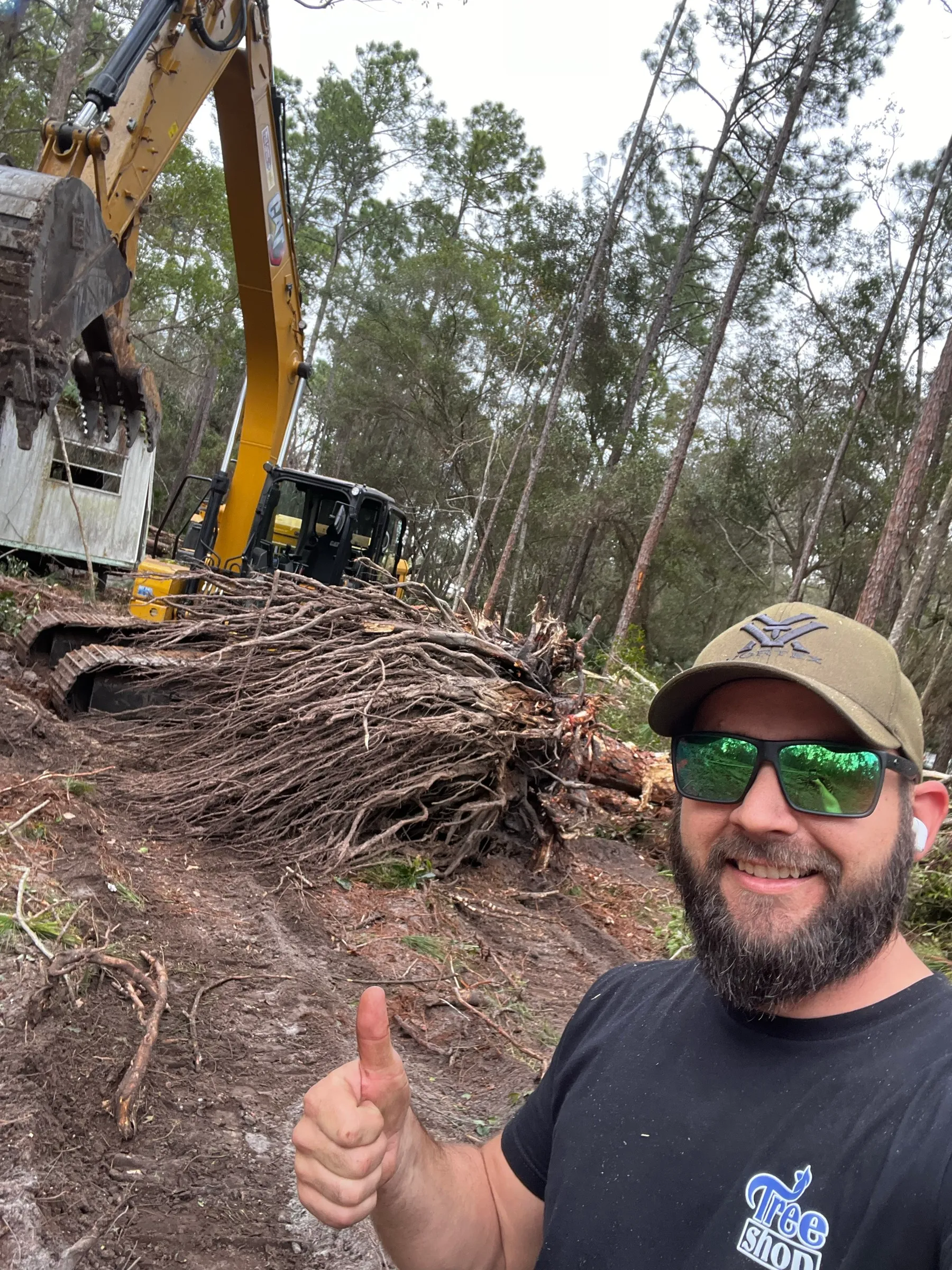 TreeShop owner Jeremiah Anderson with massive root ball after stump extraction — owner-operated land clearing